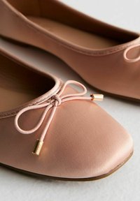 Rosa satinballetskor med fyrkantig tå, dekorerade med en bård av guldfärgad hårdvara och en slät, matt yta.