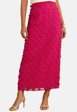 Falda fucsia con un patrón floral texturizado, presentando una silueta recta y una abertura lateral. Combinada con tacones dorados con tiras.