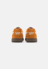 Reebok-sneakers i orange mocka med bruna accenter, vit logotyp och vadderad sula. Designade för komfort och stöd.