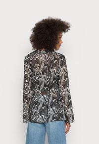 Blusa transparente em preto e branco com efeito mármore e mangas longas. Apresenta um decote alto e um design fluido. Usada com jeans azul claro.