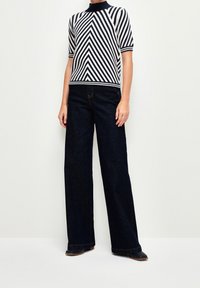 Pruhovaný pletený top v krémové a námořnické barvě s vyvýšeným límcem, kombinovaný s volnými tmavými džíny. Džíny mají klasický design s pěti kapsami.