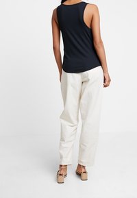 Navy ribbed tank top, loose-fitting cream pants, and beige block-heeled sandals. Minimalist design, smooth texture, and simple accents.