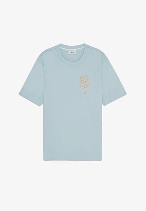 Vaaleansininen puuvillashirt, jossa on pyöreä kaula-aukko ja lyhyet hihat. Vasemmassa rinnassa on beige kukkakirjonta.