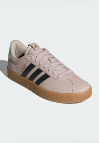 Svetle růžové tenisky s černými třemi pruhy, texturovaný svršek, flexibilní gumová podrážka a zlatý logo detail na jazyku. Neformální a nízkoprofilový design.