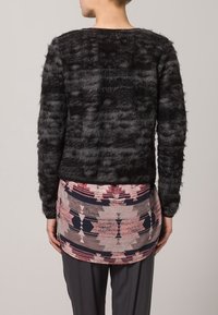 Suéter negro de felpa con un patrón texturizado, combinado con una falda de colores multicolores que presenta diseños geométricos y una cinturilla negra.