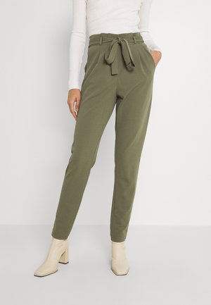 Pantalons tapered vert olive avec une taille ceinturée, faits d'un tissu doux, associés à des bottines à talons carrés couleur crème.