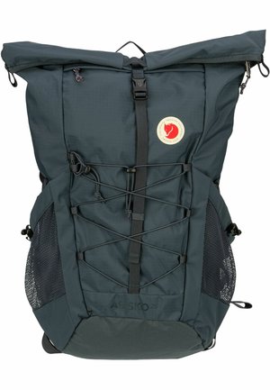 Dark green fabric backpack with roll-top closure, front bungee cords, side mesh pockets, and logo patch. Sturdy and lightweight design.