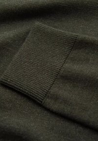 Tissu de pull vert foncé avec un détail de poignet côte. La texture semble douce et légèrement texturée, mettant en valeur des points de couture rapprochés.