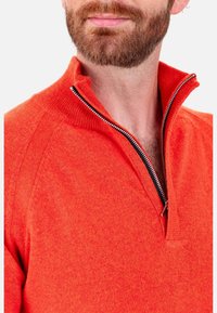 Roter Pullover mit halbem Reißverschluss aus gestricktem Stoff. Verfügt über einen hohen Kragen mit kontrastierendem Reißverschluss. Glatte Textur mit subtilem meliertem Muster.