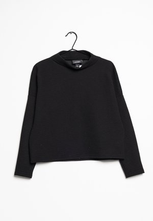 Černý zkrácený svetr s ribovanou texturou, vysokým límcem a dlouhými rukávy. Visí na černém háčku proti bílému pozadí.