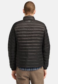 Giacca a vento nera con design trapuntato e strisce orizzontali. Collo alto e polsini elasticizzati. Sottile logo del marchio sulla parte superiore della schiena.