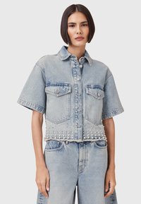 Lichtblauwe denim cropped jack met korte mouwen, twee borstzakken, parelversieringen langs de zoom en een knoopsluiting.