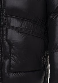 Schwarze Daunenjacke mit glänzender Oberfläche, gestepptem Design und einer geräumigen Brusttasche mit Klappe. Mit Reißverschluss und elastischen Akzenten.