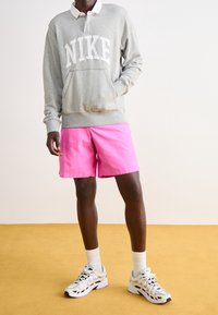 Gray sweatshirt with white "NIKE" logo, pink shorts, and white socks paired with gray and white sneakers on a yellow floor.