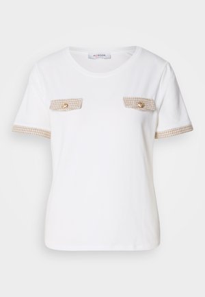 Camicetta bianca a maniche corte con rifiniture a scacchi beige sui lati e tasche a soffietto sul petto, ciascuna delle quali presenta un bottone dorato.