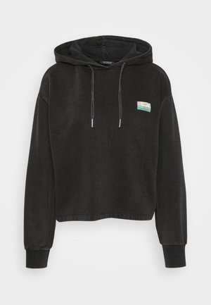 Black cropped hoodie made from soft fabric, featuring a kangaroo pocket, drawstring hood, and a small colorful patch on the front.