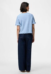 Light blue knit sweater with short fringed sleeves, paired with high-waisted dark denim wide-leg pants. Simple, textured design.