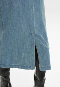 Gaiša zila džinsu svārki ar sānu iegriezumu, ar taisnu piegriezumu un redzamām šuvēm. Valkāti ar melniem līdz ceļiem zābakiem.