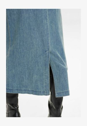 Világoskék farmer szoknya oldalsó hasítékkal, egyenes szabással és látható varrással. Fekete, térd fölé érő csizmával viselve.