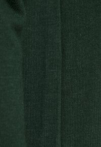 Tissu en tricot côtelé vert foncé avec une couture verticale au centre, montrant une texture fine et des détails de couture.