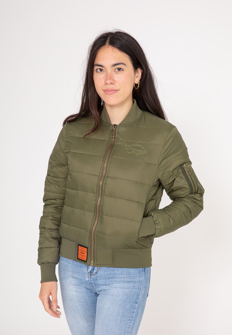 Oliwkowa, pikowana kurtka bomberka z zapięciem na zamek, ściśniętymi mankietami i pomarańczową metką na dole. Posiada boczne kieszenie i ozdobne przeszycia.
