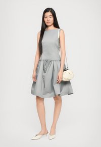 Szürke ujjatlan ruha, összefogott derékkal, bő szoknyával és térd hosszúsággal. Fehér táskával és krémszínű slip-on cipőkkel van kiegészítve.