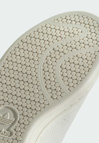 Shoe sole in off-white material featuring a textured pattern of small circles and curved lines, with a logo embossed at the heel.
