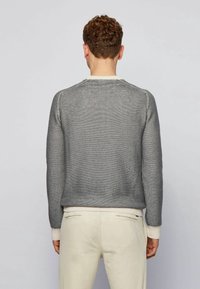 Pull en maille grise avec un motif texturé ; encolure et poignets côtelés de couleur crème. Coupe décontractée, présenté de dos.