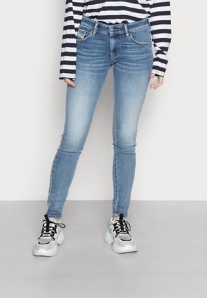 Person trägt hellblaue Skinny-Jeans, ein schwarz-weiß gestreiftes Langarmshirt und weiße klobige Sneaker mit schwarzen Schnürsenkeln.
