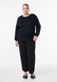 Schwarzer strukturierter Pullover mit Rundhalsausschnitt, kombiniert mit lockeren schwarzen Hosen und schwarzen Ballerinas mit einer geflochtenen Detail.