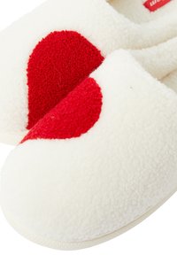 Białe kapcie z polaru z dużym czerwonym sercem o fakturowanej powierzchni, zaokrąglonym kształtem czubka i miękką, pluszową powierzchnią. Gumowa podeszwa.