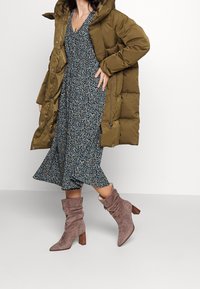 Oliivinvihreä puffatakki, sinivalkoinen kukkakuosisettu mekko ja vaaleanharmaat löysät nilkkasaappaat puukorkoilla.