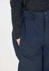 Pantalons imperméables bleu marine avec une texture lisse, dotés d'une large taille, de deux poches latérales et de fermetures à bouton à l'avant.