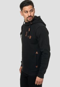 Sudadera negra hecha de material suave, con un bolsillo tipo canguro, cordones y detalles en cuero marrón en los bolsillos y cremalleras.