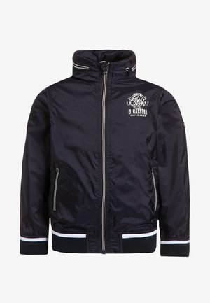 Granatowa kurtka z zamkiem na wysokości kołnierza, z przednimi kieszeniami, białymi paskami na mankietach oraz białym napisem "D. Gaastra Sailmaker" na klatce piersiowej.