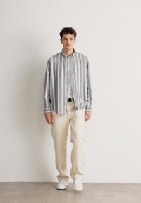 Cămașă albă cu dungi gri, cu un buzunar pe piept, asociată cu pantaloni de culoare crem și adidași albi. Design simplu, casual.