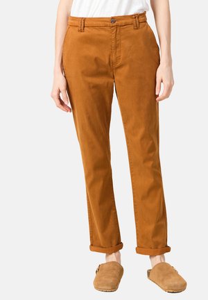 Brown cotton chinos with a slim fit, featuring a button closure, belt loops, and folded cuffs, paired with light brown slip-on shoes.
