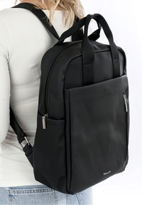 Sac à dos noir en tissu lisse, doté de deux poignées supérieures, de bretelles réglables, d'une poche zippée à l'avant et d'un design minimaliste.