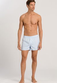 Boxers en coton à carreaux bleu clair avec taille élastique et bouton, portés par un mannequin masculin avec un torse nu.