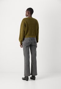 Ελιόχρωμος, φuzzy πλεκτός σεντόνι με fitted μέση. Γκρι παντελόνι σε φαρδιά γραμμή με ορατές πίσω τσέπες. Μαύρες μπότες έως τον αστράγαλο συμπληρώνουν το σύνολο.