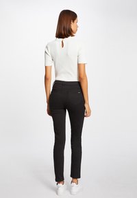Witte geribbelde top met korte mouwen, met een sleutelgatdetail aan de achterkant; gecombineerd met zwarte strakke broek en witte sneakers. Eenvoudig en schoon ontwerp.