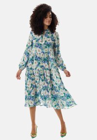 Floral midi dress with long sleeves, featuring a green and blue pattern, lightweight fabric, and a tie neckline; flowy silhouette.