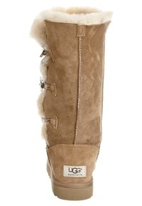 Brązowy zamszowy kozaki do kolan z futrzanym podszyciem, z trzema zapięciami na klamerkę i płaską podeszwą. Logo UGG na pięcie. Miękka tekstura.
