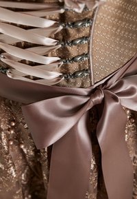 Corset with a textured bronze fabric, detailed with satin ribbons, beaded accents, and prominent bow at the waist. Decorative closures visible.