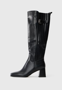 Bota de piel negra hasta la rodilla con tacón cuadrado, correa de hebilla lateral y panel cosido vertical en la parte trasera.