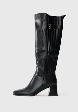 Black knee-high leather boot with block heel, side buckle strap, and vertical stitched panel on the back.