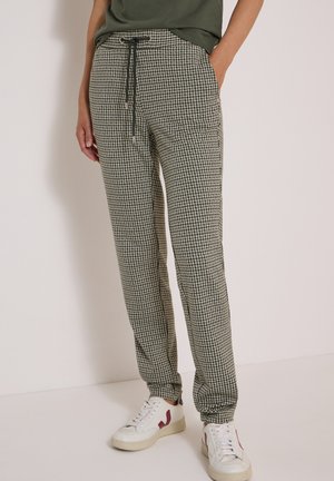 Personne portant un pantalon de jogging à motif pied-de-poule noir et blanc avec un cordon noir et des baskets blanches avec des accents rouges.