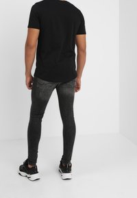 Camiseta negra de manga corta combinada con jeans skinny gris oscuro y zapatillas deportivas negras. El fondo es blanco liso.