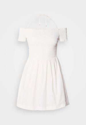 White off-the-shoulder dress with smocked bodice, short sleeves, and gathered skirt. Made of lightweight cotton material. Ties at neckline.