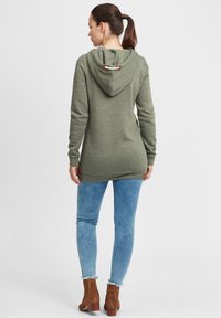 Olivgrön lång hoodie med dragsko i huvan, ribbade ärmslut och nederkant. Matchas med ljusblå slim fit-jeans och bruna ankelstövlar.
